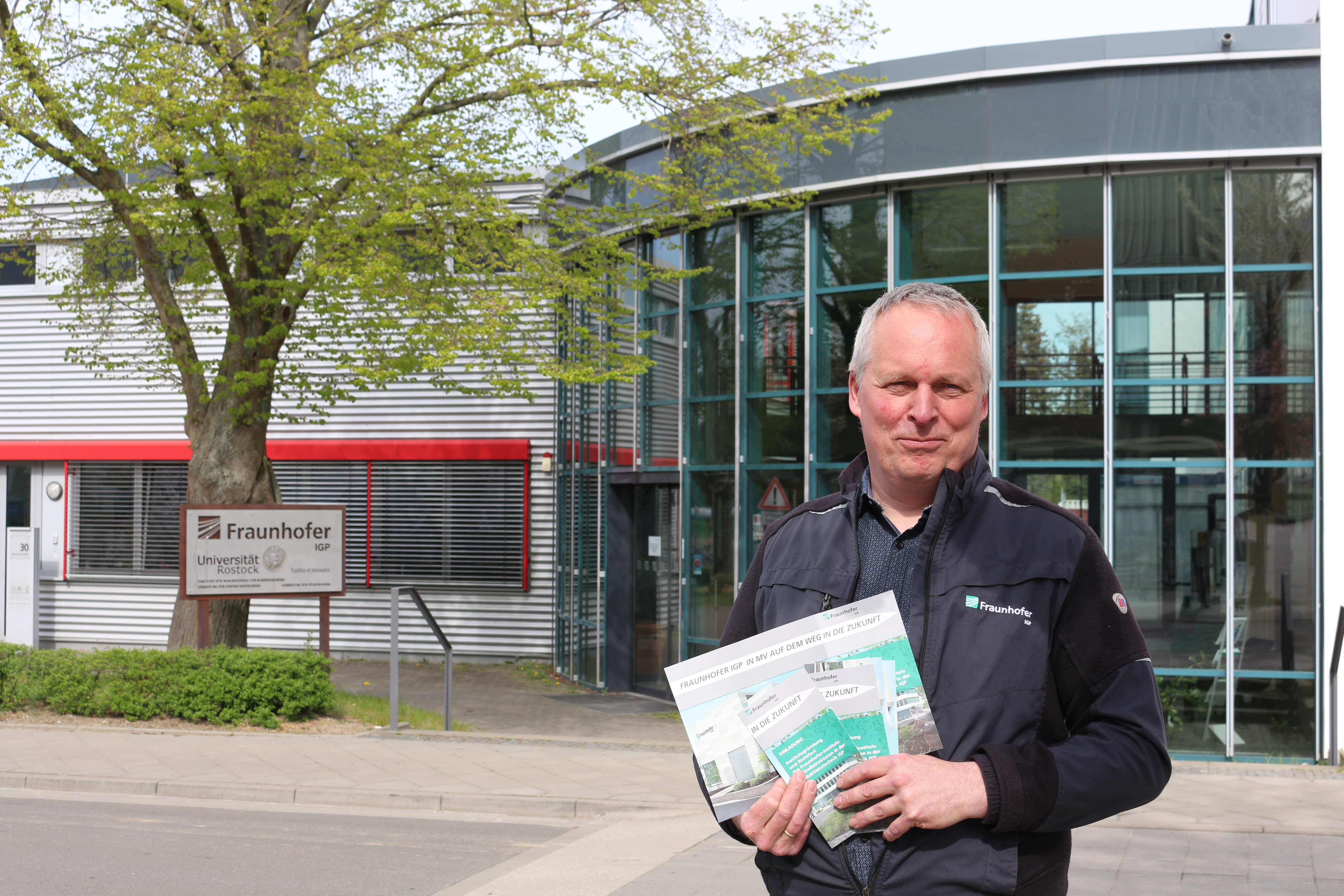 Prof. Flügge steht vor dem Institut und hält Einladung für die Feierlichkeit. 