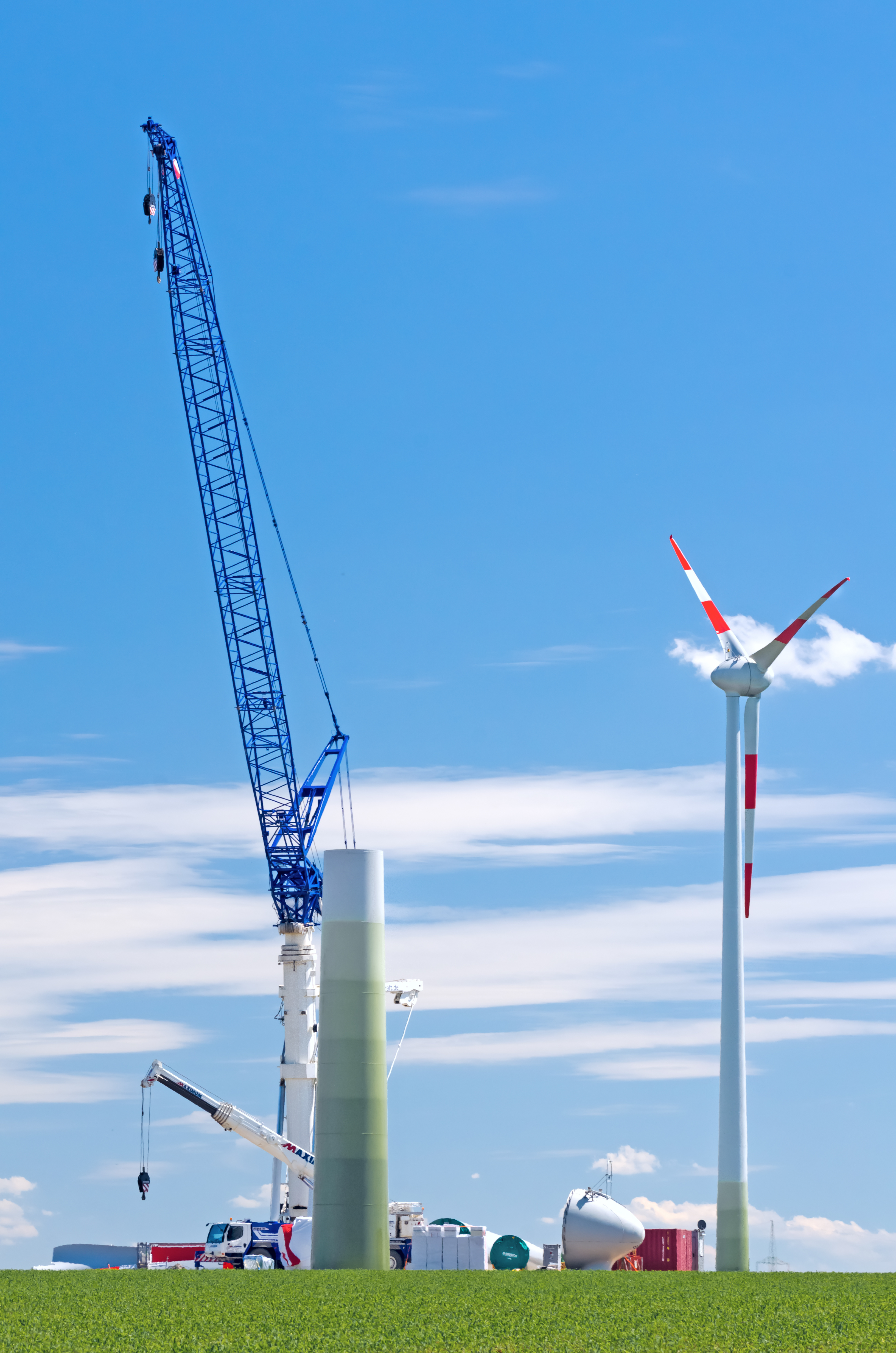 Ein blauer Kran und Windrad auf einer Wiese während den Bauarbeiten für die Aufstellung eines zweiten Windrads.